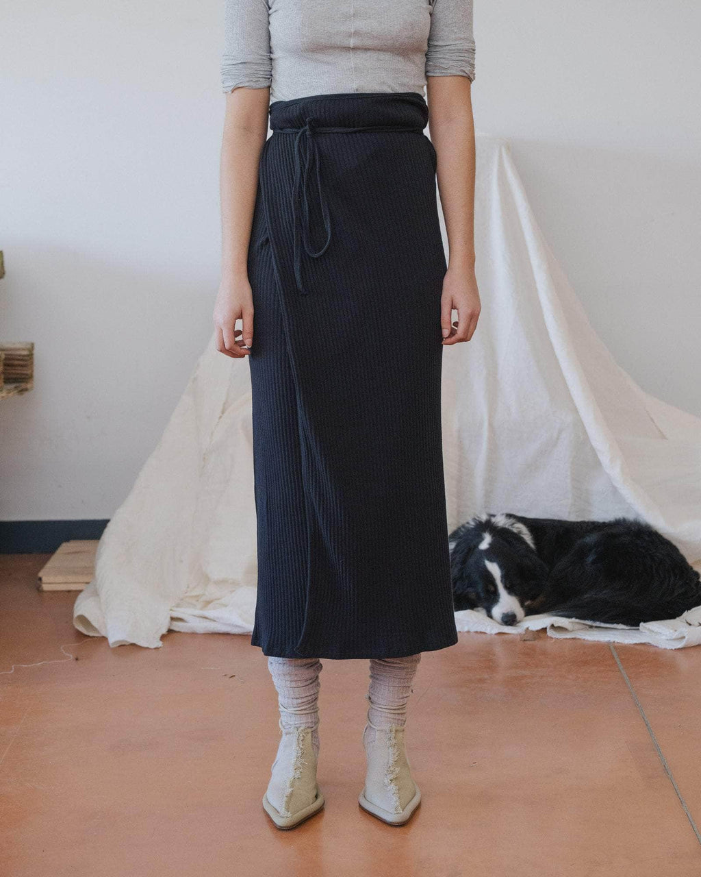 Person wearing a long dark skirt with a dog lying on the floor in the background.