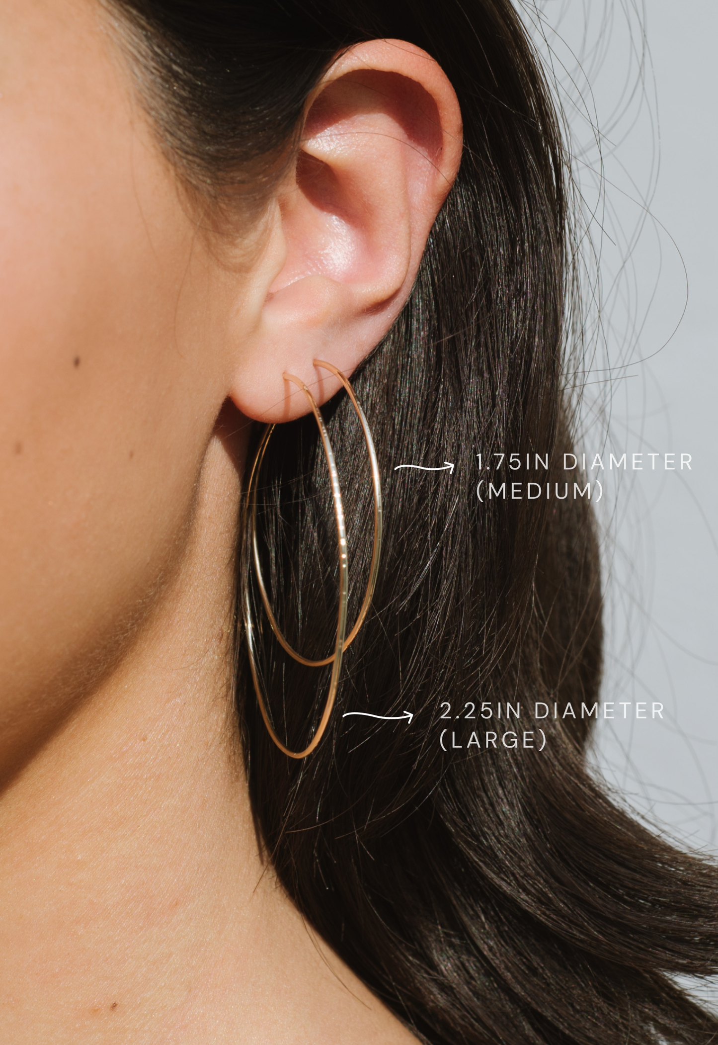 Close-up of a person wearing gold hoop earrings with size labels.