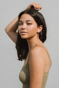 Woman with long dark hair wearing a green tank top against a light gray background