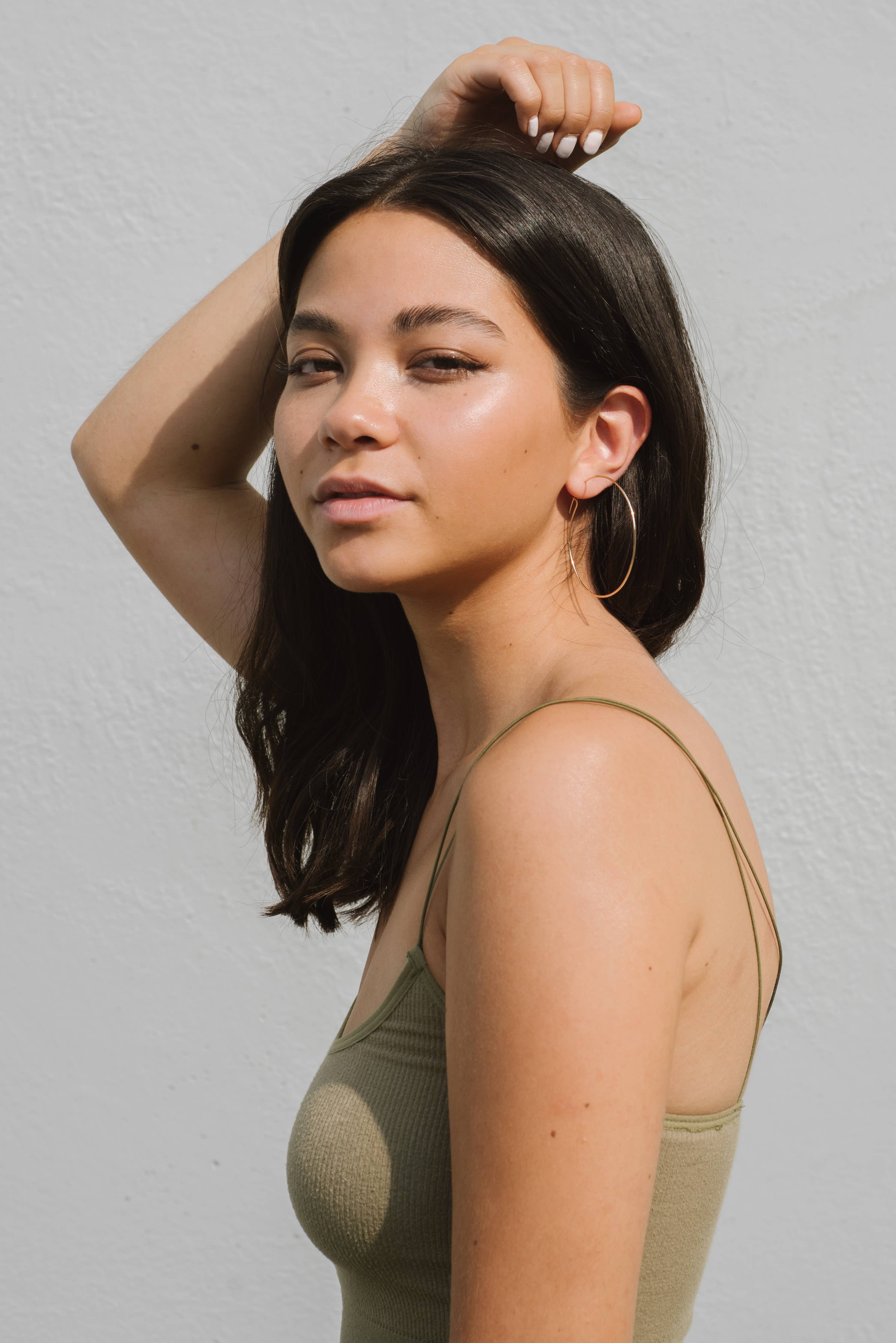 Woman with long dark hair wearing a green tank top against a light gray background